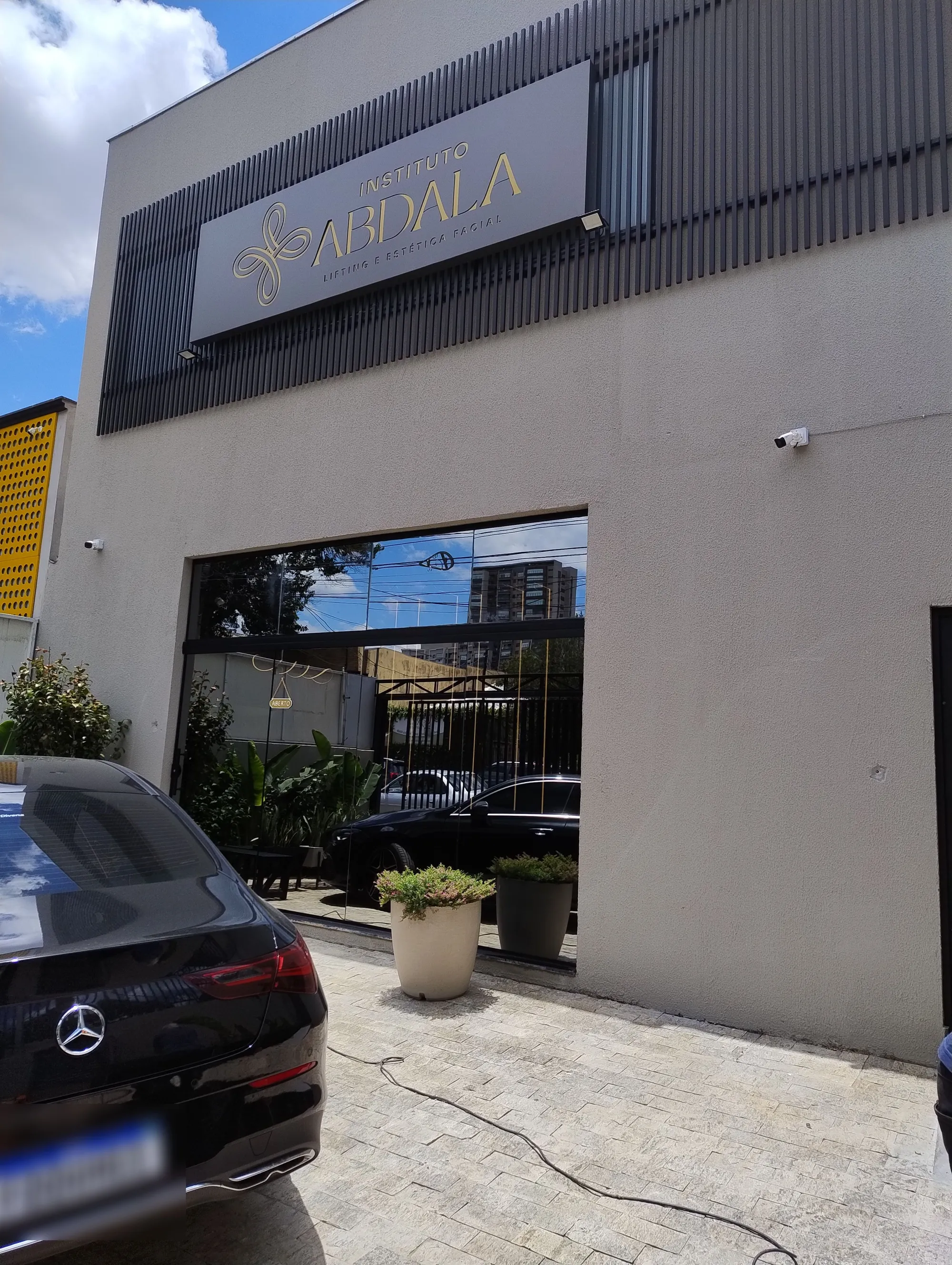 Fachada do Instituto Abdala com letreiro dourado, revestimento cinza e detalhes em ripado metálico.