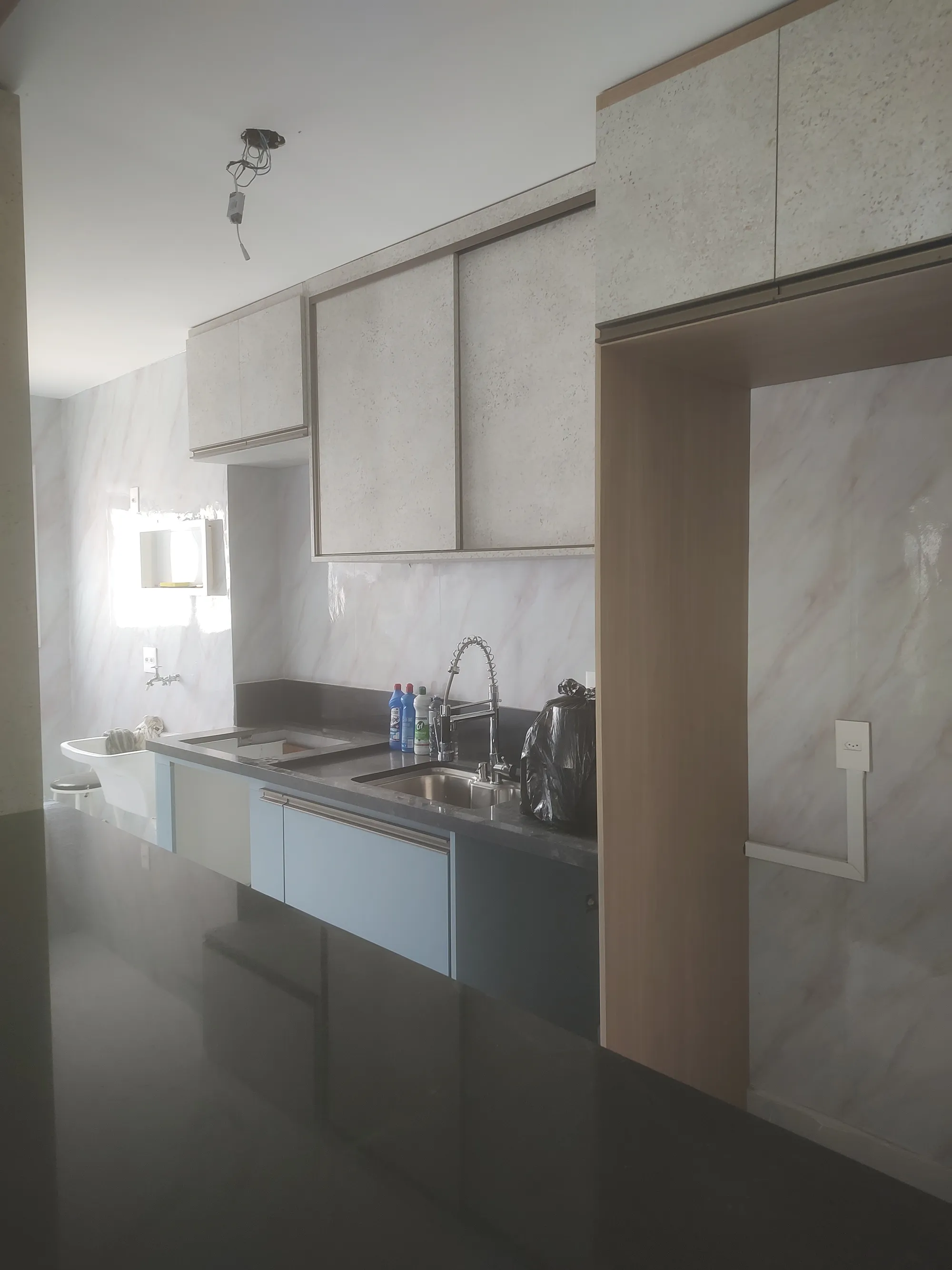 Vista interna da cozinha destacando a bancada escura, pia com torneira gourmet e armários superiores texturizados.