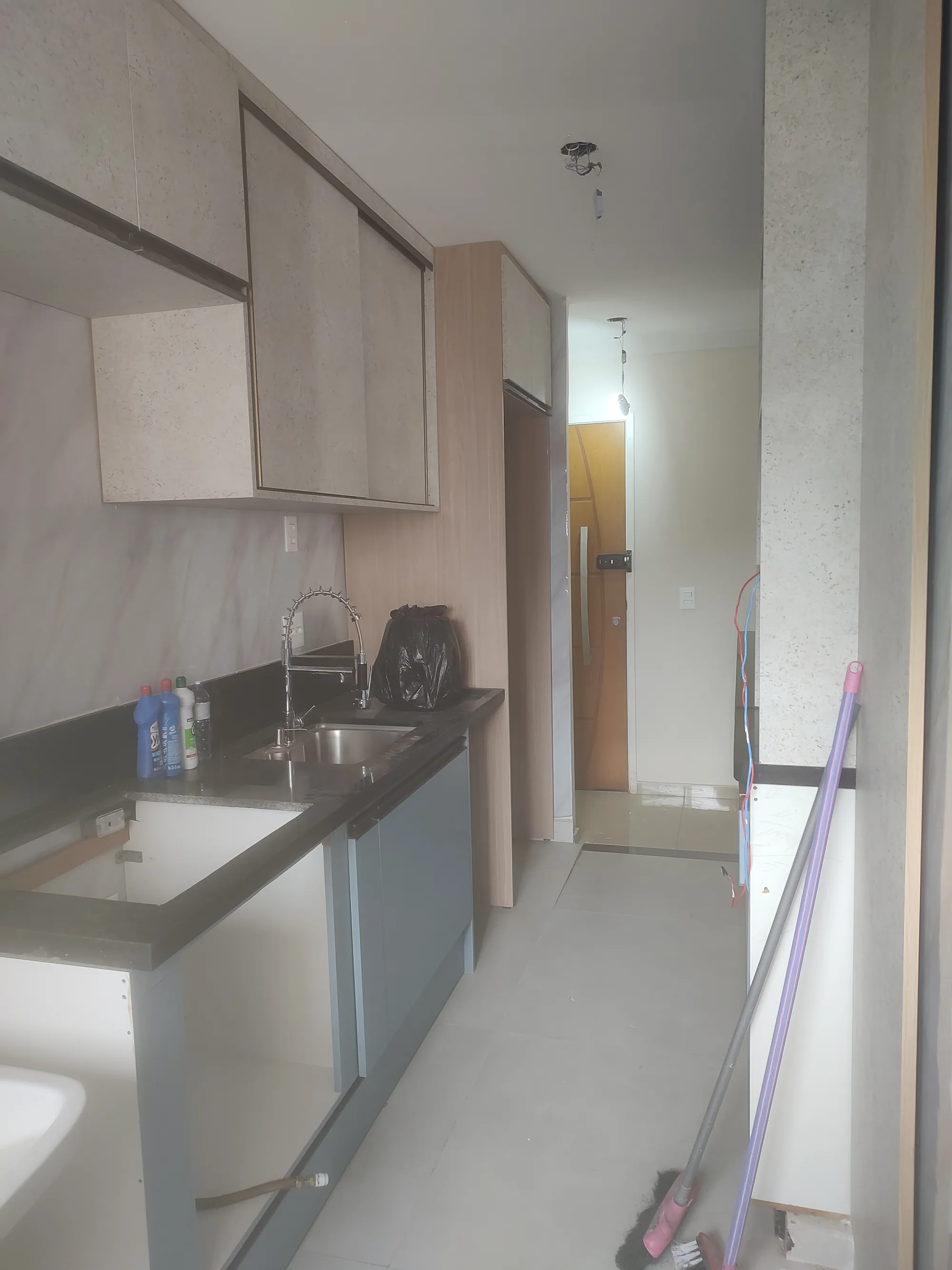 Vista geral do corredor da cozinha, mostrando a disposição dos armários até a porta de entrada.
