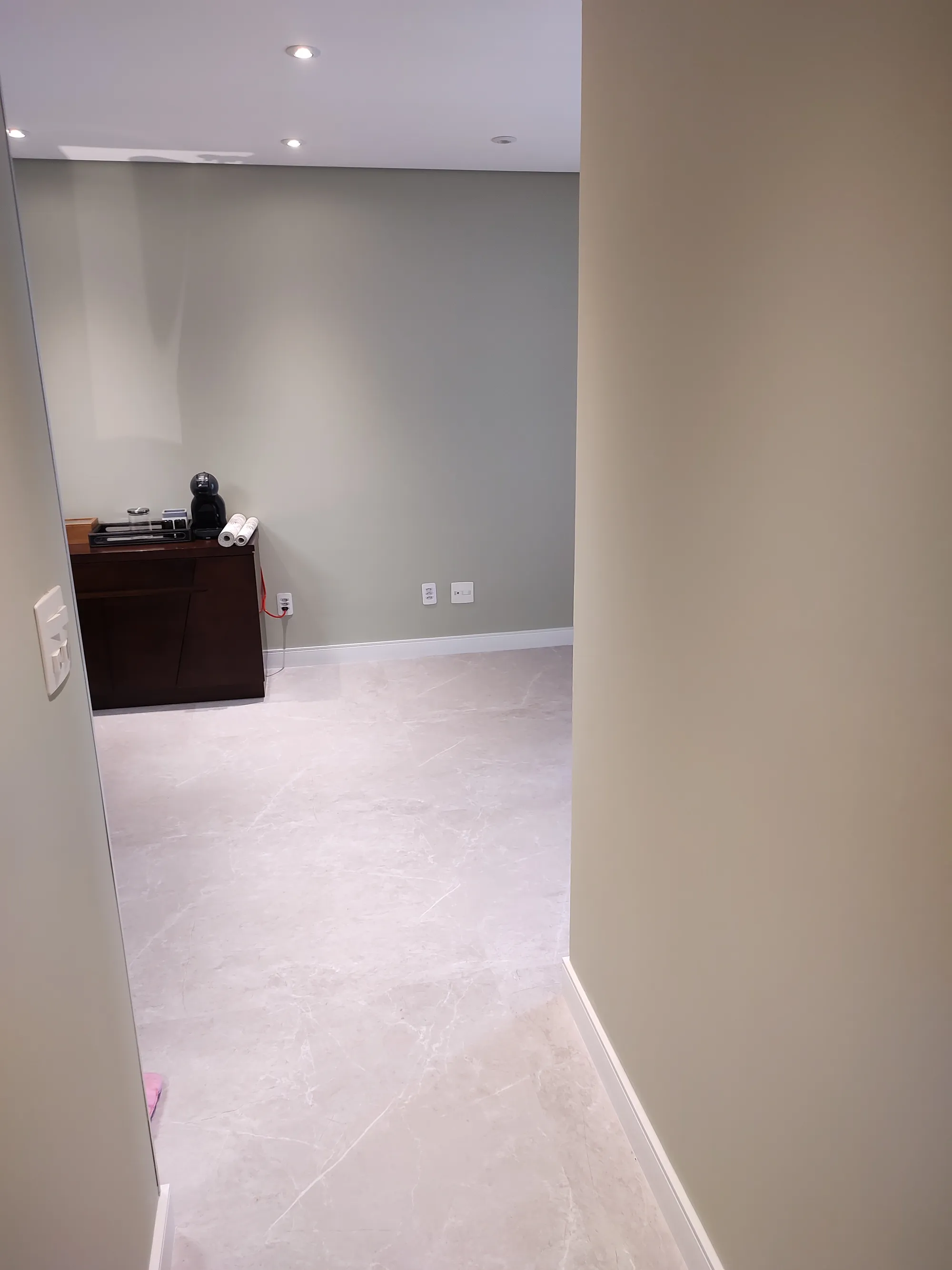 Corredor de circulação com piso de porcelanato claro marmorizado e paredes verde-claras, dando acesso a um cantinho do café ao fundo.